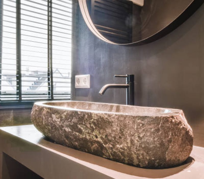 Expensive vessel sink made of natural stone with black faucet under mirror in bathroom